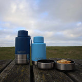 Two blue thermos bottles and a metal container on a wooden surface with a cloudy sky in the background.